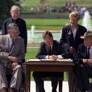 President Bush is seated at a table on the White House lawn signing a document