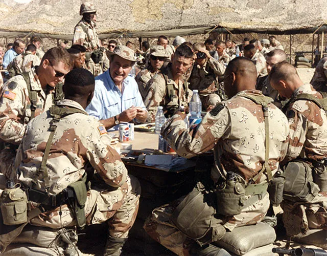President Bush is seated at a table surrounded by members of the military