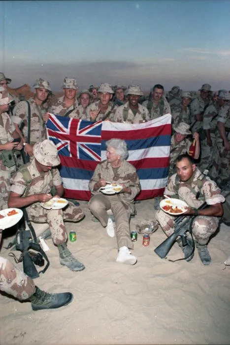 First Lady Barbara Bush sits in the sand eating Thanksgiving Dinner with Marines of the First Marine Division in Saudi Arabia