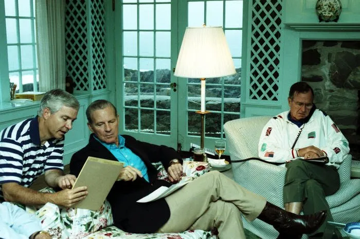 President Bush speaks to King Fahd of Saudi Arabia via telephone, at his home in Kennebunkport, Maine, as Robert Gates and Secretary Baker look on