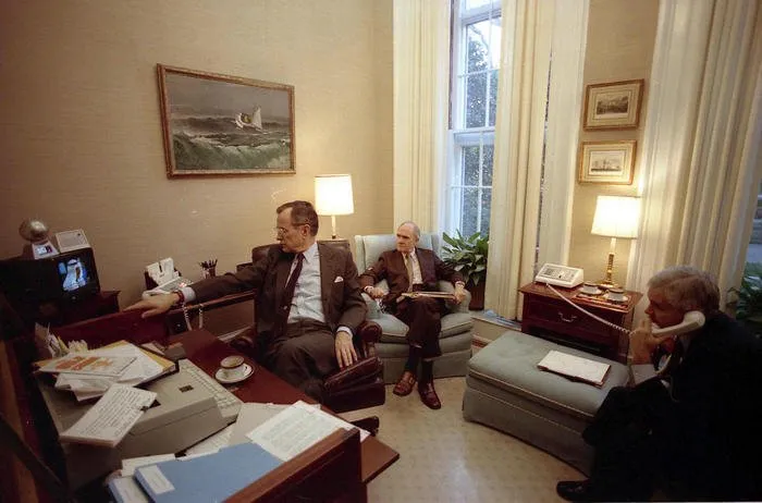 President Bush confers with Sec. James Baker (not shown), Gen. Brent Scowcroft, and Robert Gates regarding Iraq's withdrawal from Kuwait as they watch television coverage in the Oval Office Study