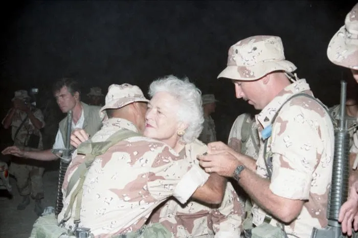 First Lady Barbara Bush hugs a Marine of the First Marine Division as another Marine pins USMC rank on her collar during her and President Bush's Thanksgiving visit with the troops in Saudi Arabia