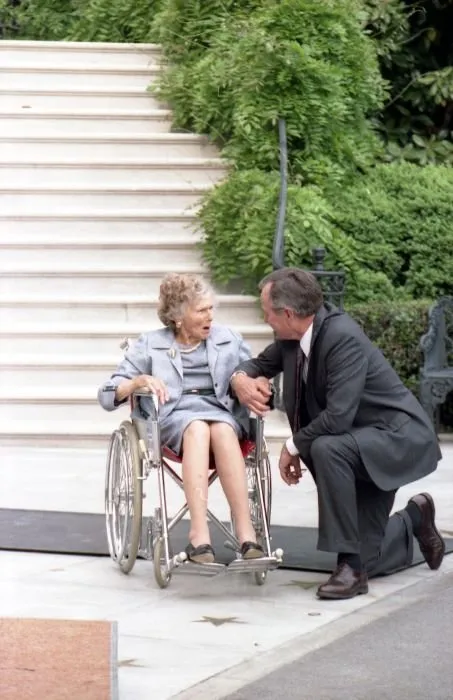 President Bush kneels and holds his mother's hand as they talk in front of South Portico