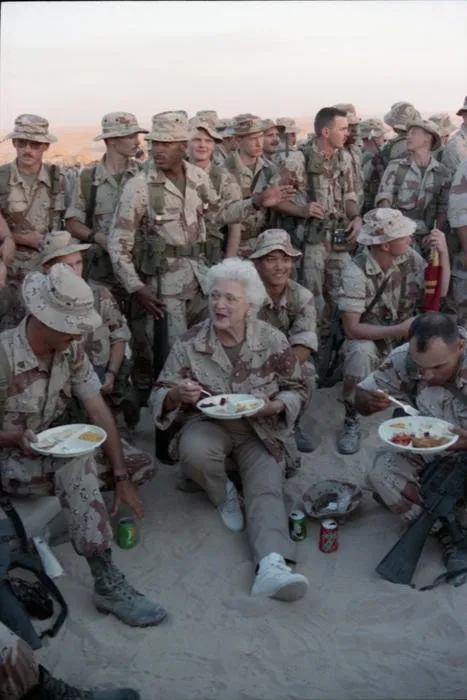 First Lady Barbara Bush sits in the sand eating Thanksgiving Dinner with Marines of the First Marine Division in Saudi Arabia