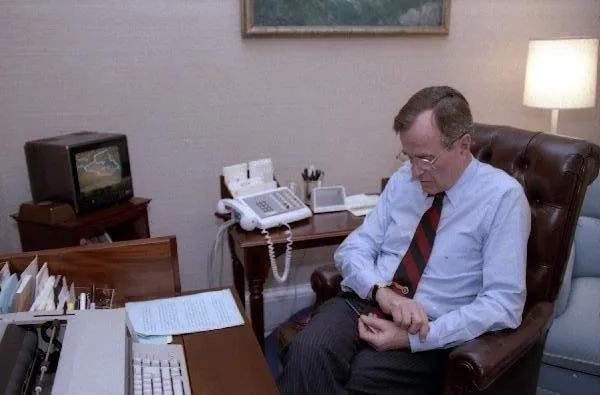 President Bush watches television as he checks his watch