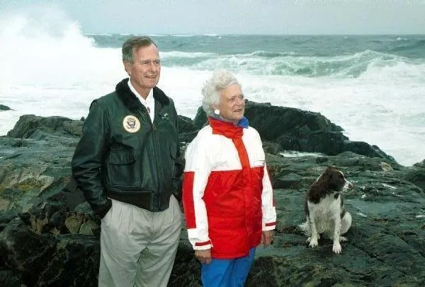 President Bush and Barbara Bush stand on rocks with Millie at Walker's Point