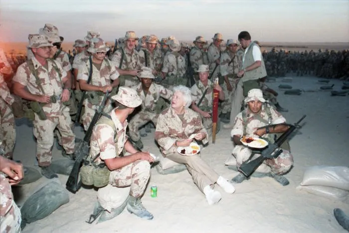 First Lady Barbara Bush sits in the sand eating Thanksgiving Dinner with Marines of the First Marine Division in Saudi Arabia