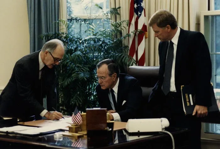 President Bush reads a document as General Scowcroft makes notations and Vice President Quayle looks on
