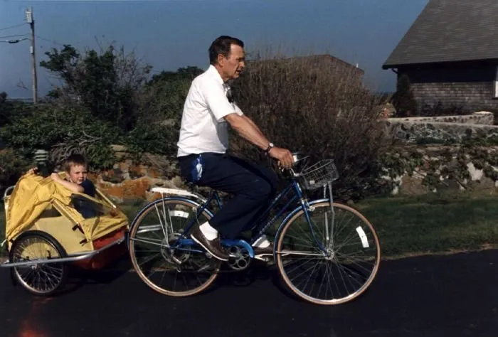President Bush rides a bicycle with his grandson, Sam Leblond, in the attached cart