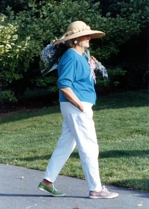 Wearing mismatched shoes, Mrs Bush carries a bunch of flowers, as she walks across the driveway